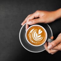 Cappuccino in woman hands on dark black background