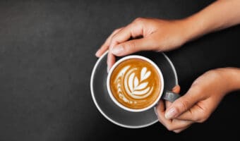 Cappuccino in woman hands on dark black background